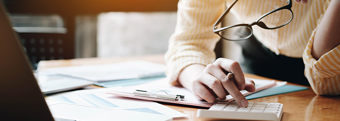 Woman leaning over financial documents and using a calculator with her glasses in hand