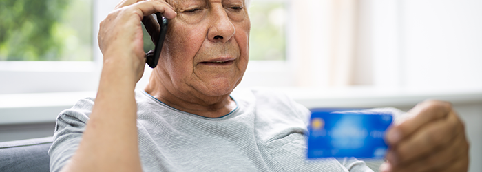 Older man on the phone holding a credit card in front of him.