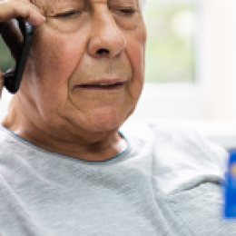 Older man on the phone holding a credit card in front of him.