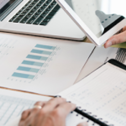 Two people sitting in front of table with reports on it and one person is writing