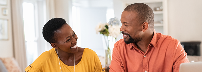 Man and woman sitting at table at home smiling at each other.