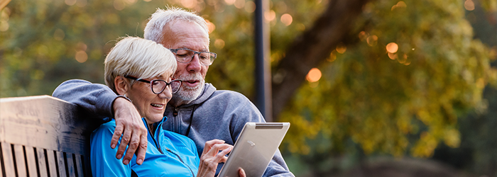 Senior man and woman sitting on a bench outside looking at a tablet together