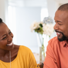 Man and woman sitting at table at home smiling at each other.