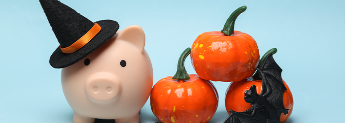 Piggy bank with a witch's hat, and orange ceramic pumpkins and a black bat next to it