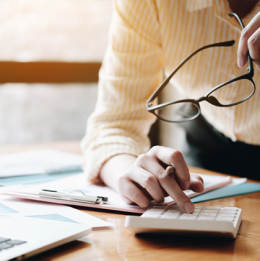 Woman leaning over financial documents and using a calculator with her glasses in hand