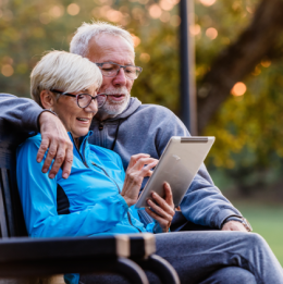 Senior man and woman sitting on a bench outside looking at a tablet together